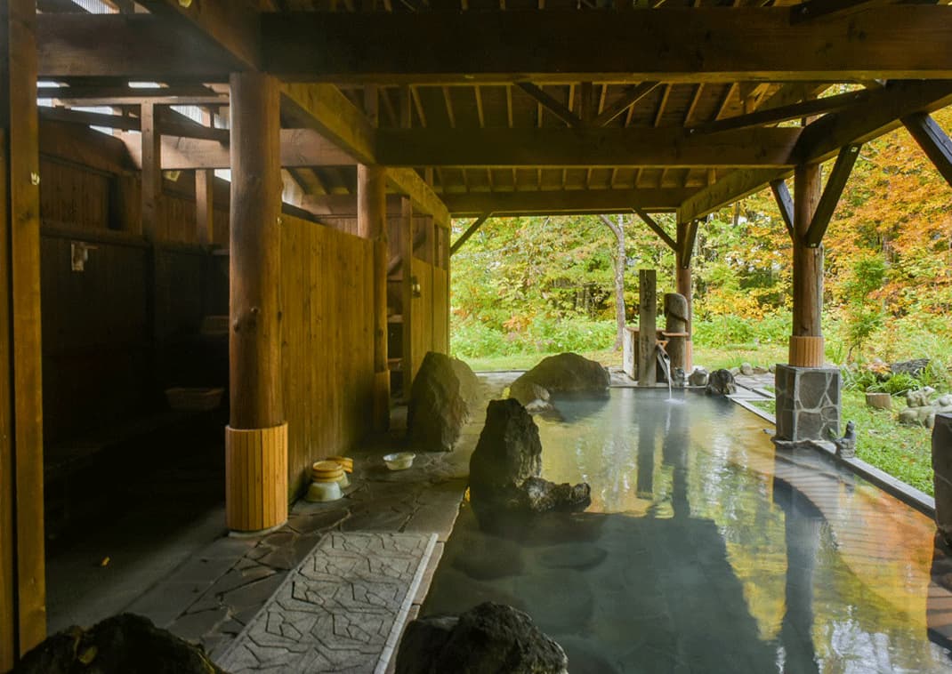 Dampen stiger op fra en udendørs onsen (varme kilder) ved en ryokan i Nyutō-skoven, Akita, Japan