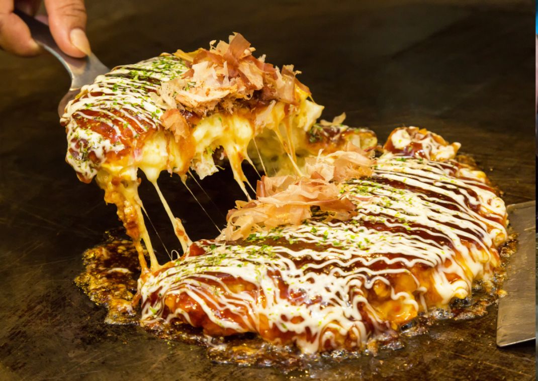 Japansk madpandekage kaldet okonomiyaki bliver tilberedt på en varmeplade
