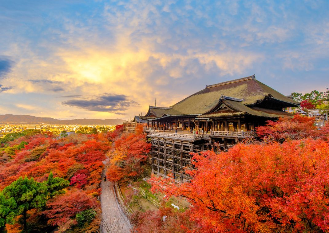 Kiyomizu-dera-templet i Kyoto omgivet af farverige røde efterårstræer under en dramatisk himmel.
