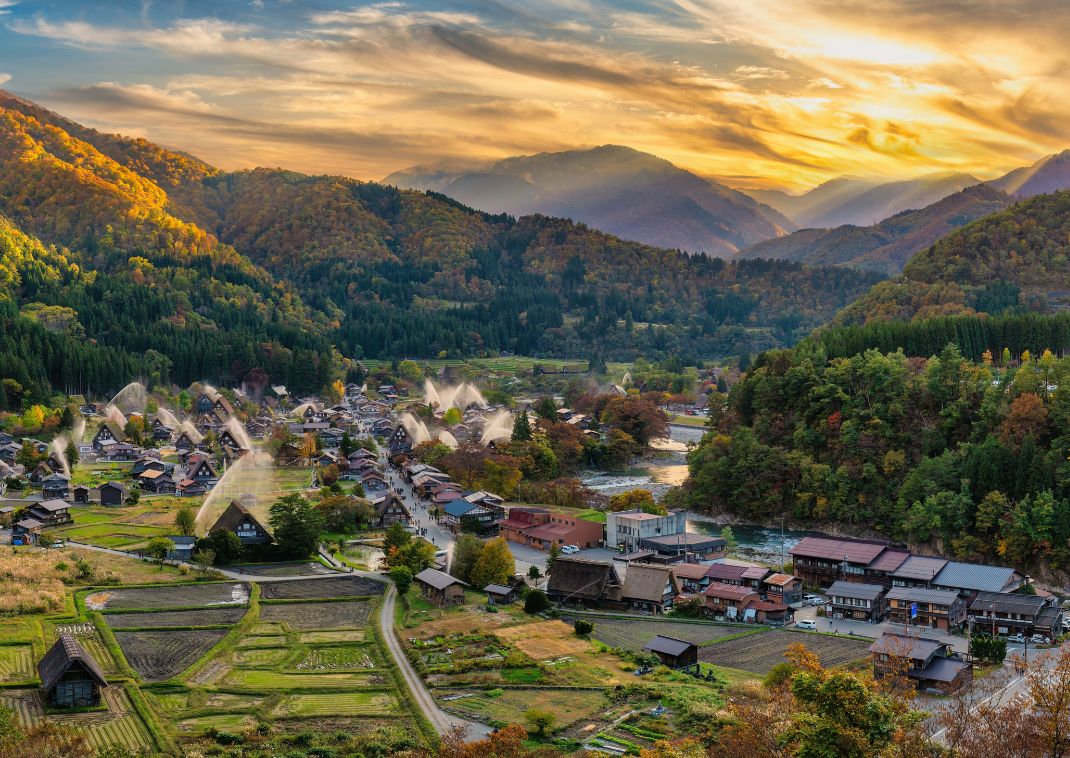 Traditionelle stråtækte huse i Shirakawa-go landsby omgivet af efterårsløv og bjerge ved solnedgang i Japan.