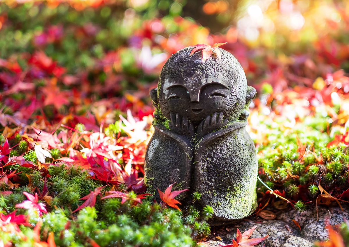 Jizo-statue med et faldende rødt ahornblad i Enkoji-templets japanske have i Kyoto.