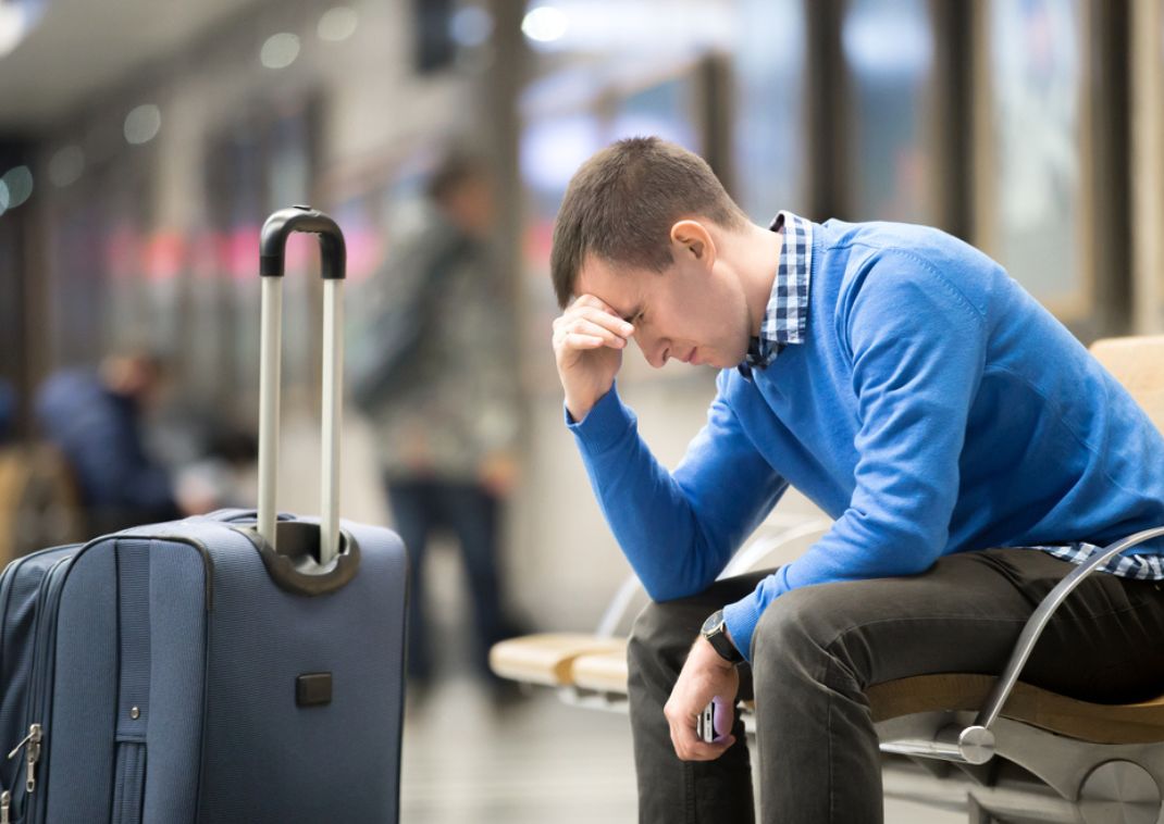 En mand sidder frustreret i lufthavnen med sin bagage fordi han ikke nåede sit fly 