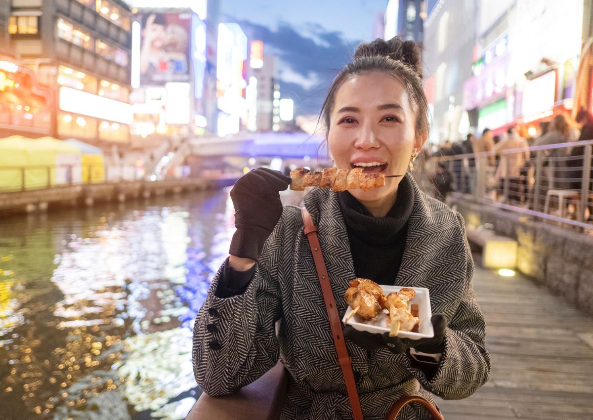 Ung kvinde spiser kyllingespyd i Dotonbori, Osaka, Japan