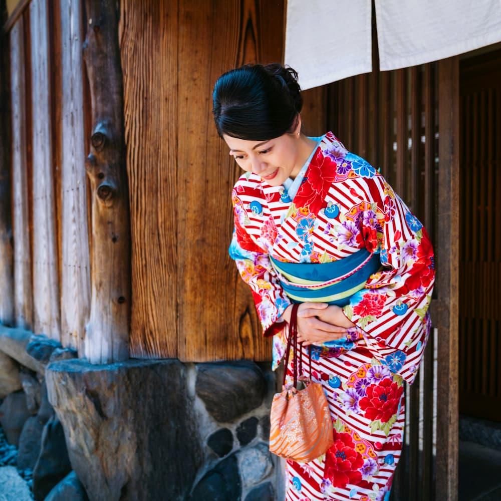 Japansk kvinde i farverig kimono bukker foran en traditionel træbygning i Kyoto