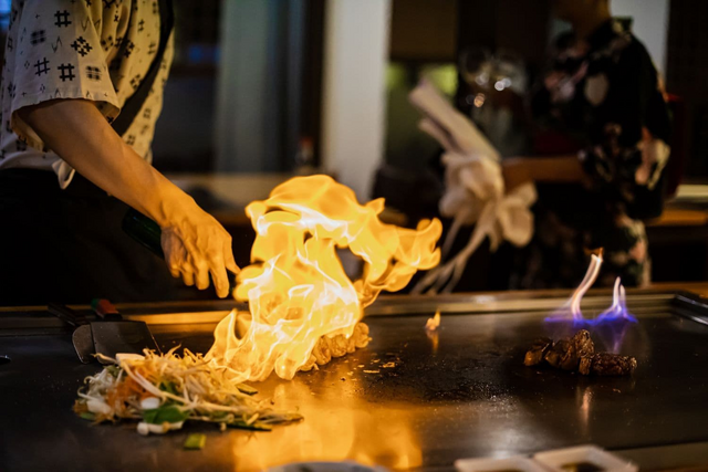En kok tilbereder et teppanyaki-måltid, med oksekød og grøntsager.