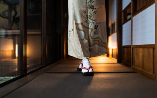 Kvinde i kimono går gennem en traditionel ryokan med tatamimåtter og shoji-døre