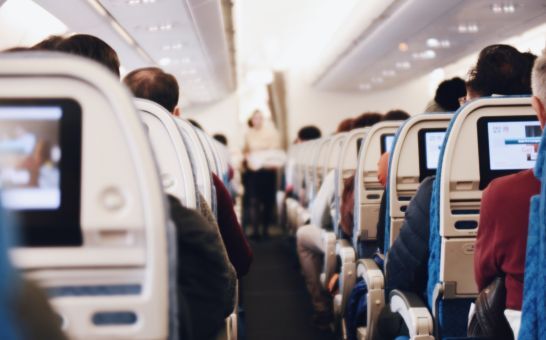 Interiør i et stort passagerfly med siddende mennesker og en stewardesse i uniform, der går ned ad midtergangen