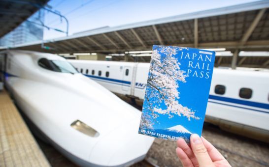Hånd med en Japan Rail Pass-billet foran en Shinkansen på Tokyo Station