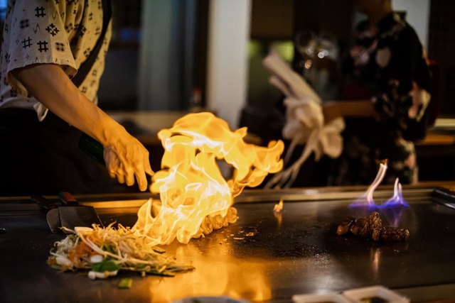 En kok tilbereder et teppanyaki-måltid, med oksekød og grøntsager.