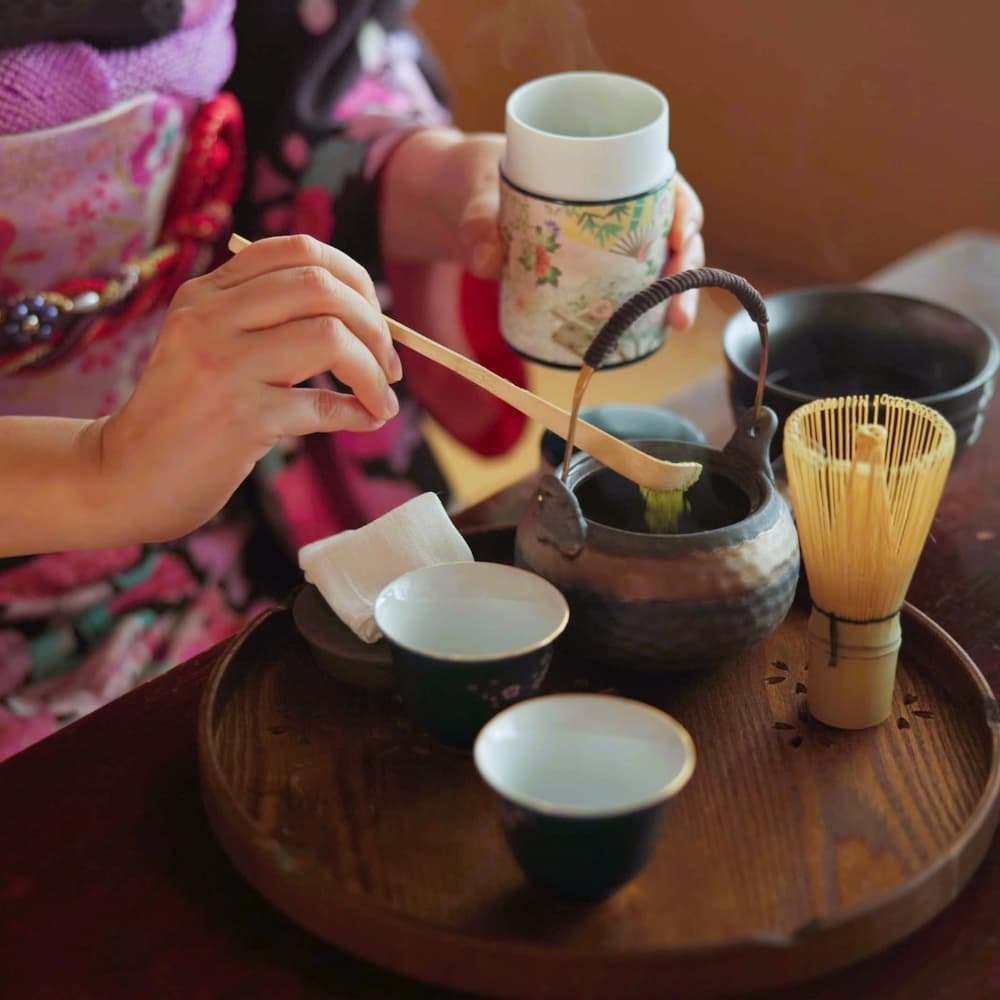 Japansk kvinde tilbereder matcha-te i en traditionel teceremoni derhjemme med matchapulver, urter og en tekande