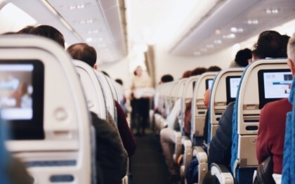 Interiør i et stort passagerfly med siddende mennesker og en stewardesse i uniform, der går ned ad midtergangen