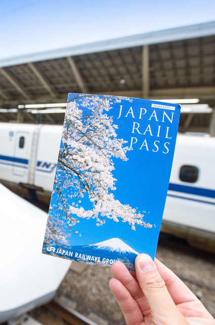 Hånd med en Japan Rail Pass-billet foran en Shinkansen på Tokyo Station