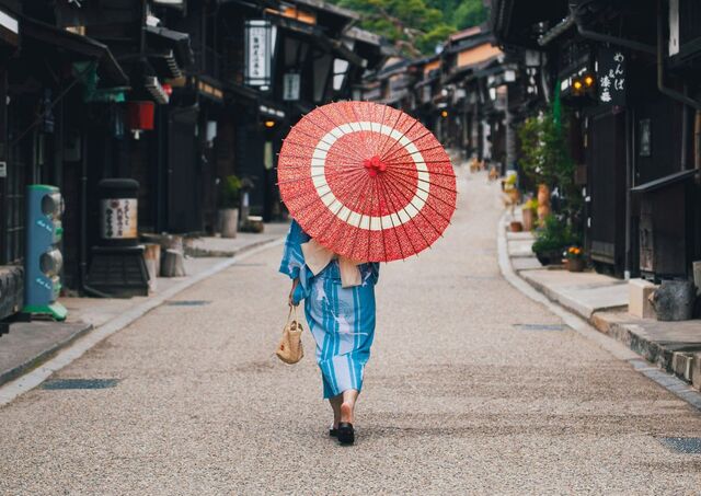 Person i kimono går gennem den historiske postby Narai i Japan med rød parasol og grønne bjerge