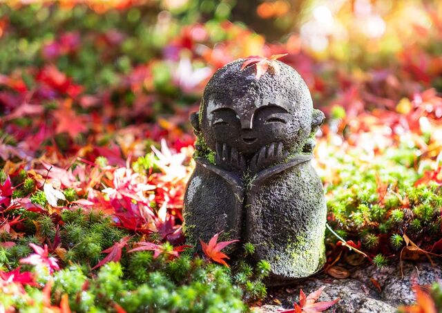 Jizo-statue med faldende rødt ahornblad i Enkoji-templets japanske have i Kyoto. 