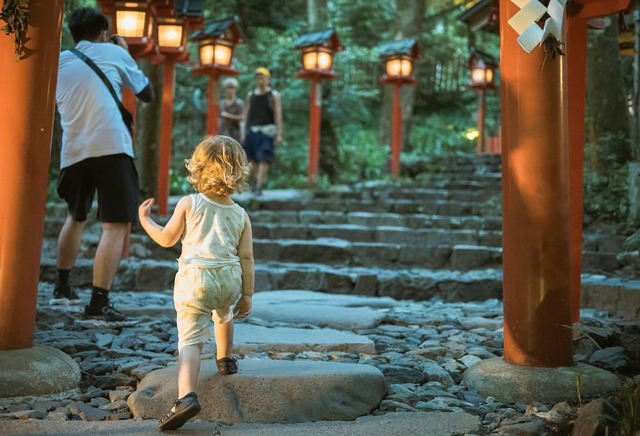Lille barn går op ad stentrappen omkranset af røde lanterner ved Kifune-helligdommen, Kyoto