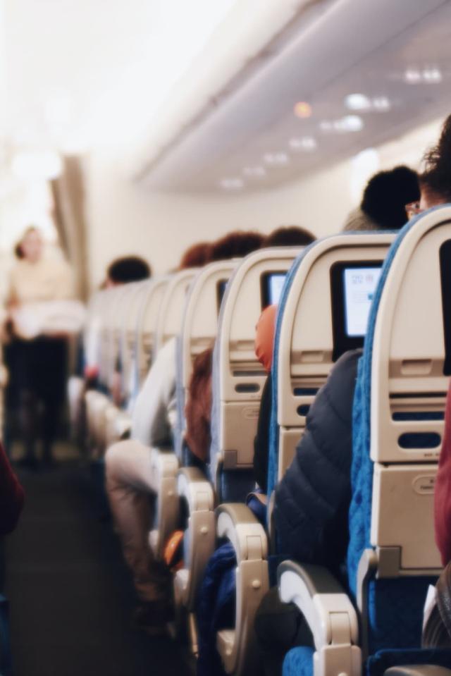 Interiør i et stort passagerfly med siddende mennesker og en stewardesse i uniform, der går ned ad midtergangen