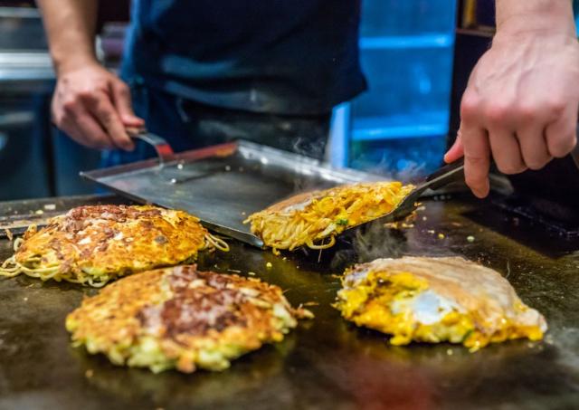 Japansk okonomiyaki under tilberedning på en varmeplade 